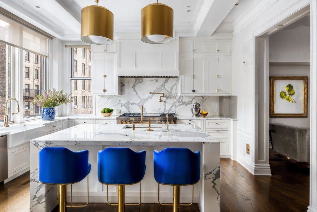 Thick marble waterfall countertop matching a backsplash in a chic kitchen by Decorilla